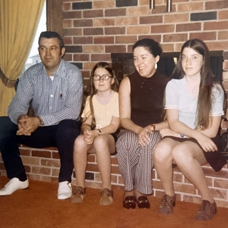 Eleanor and her family are sitting on a brick edge in front of a cozy fireplace.