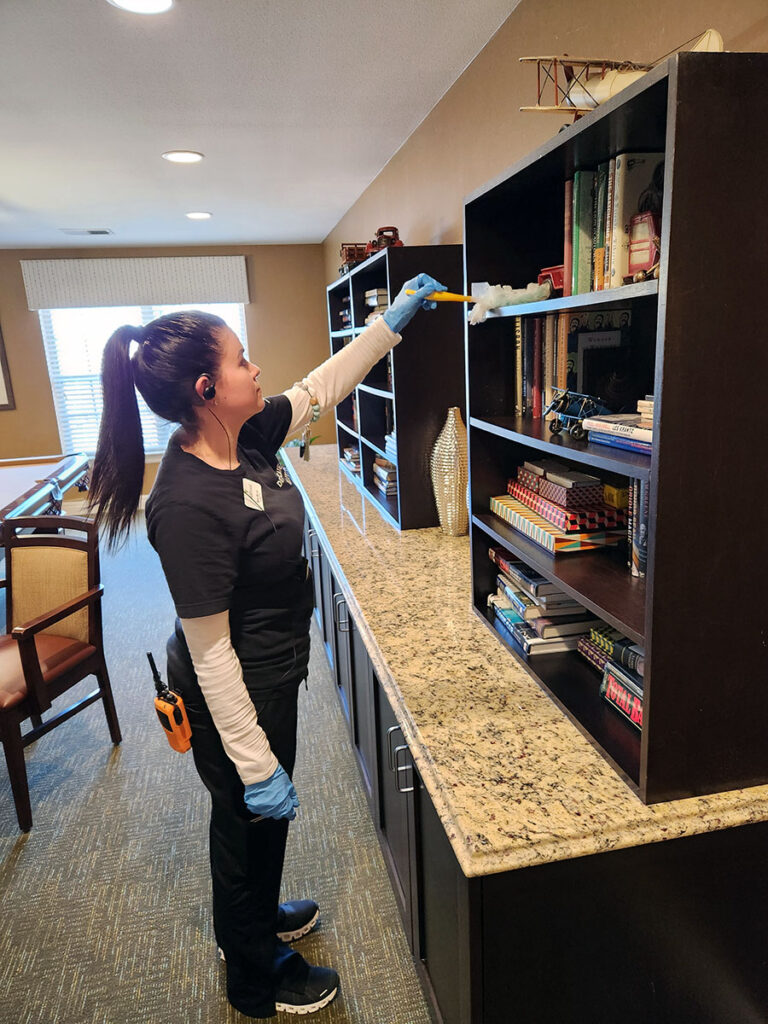 A woman in a black shirt and gloves tidying up a bookcase.