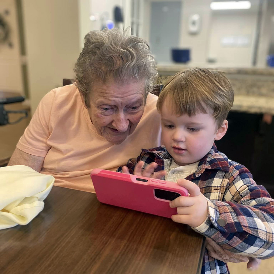 Memory care resident and child happily looking at a cell phone, sharing a joyful moment.