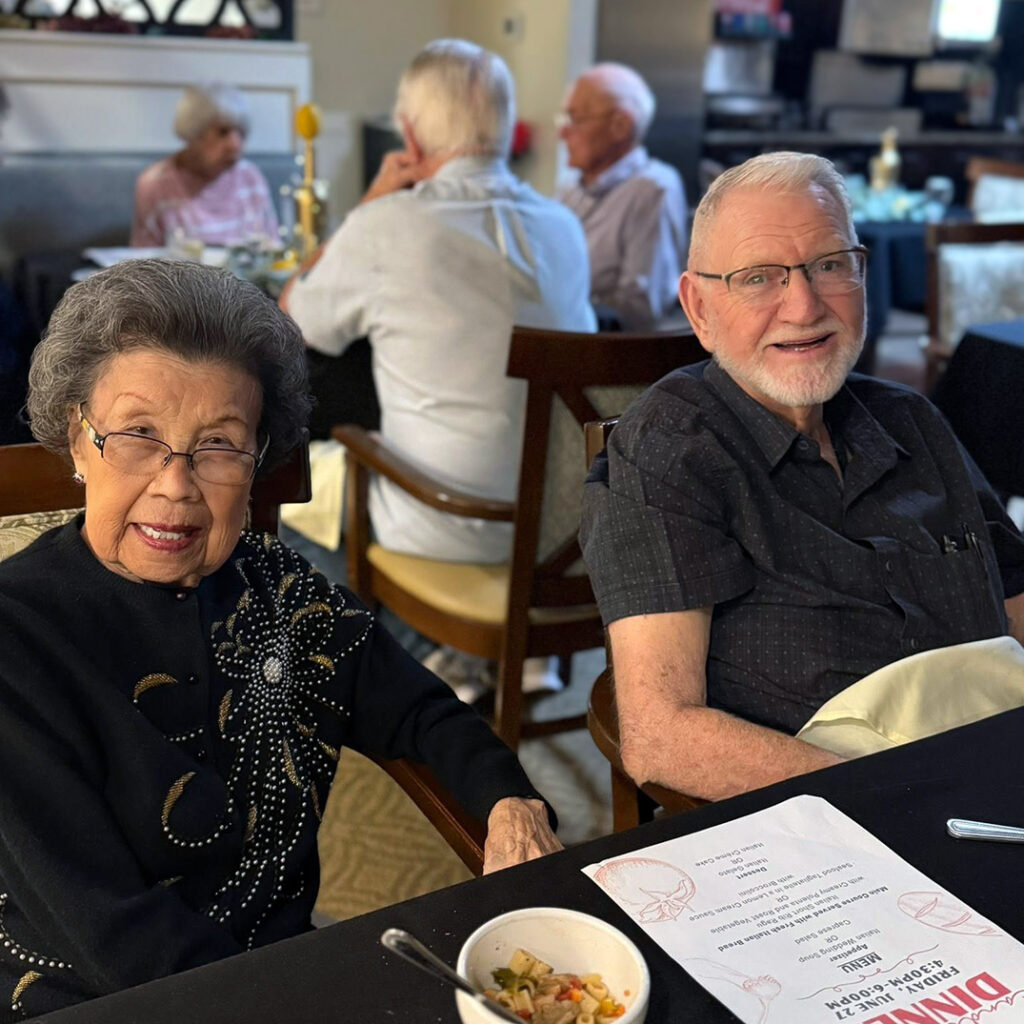 Senior couple smiles at a dining table together with a menu between them.
