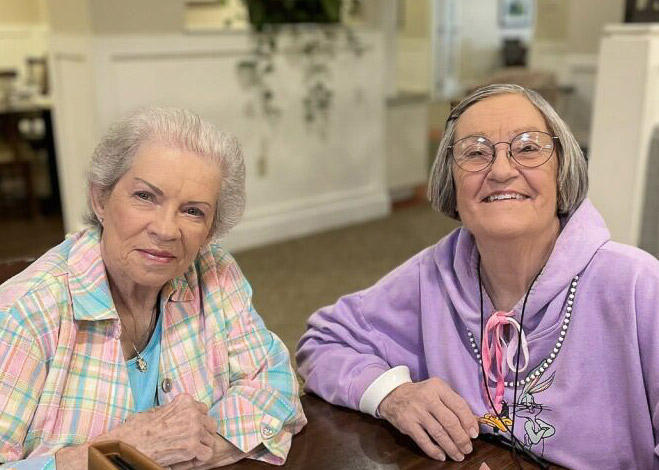 Two senior women smile during conversation in a relaxed moment.