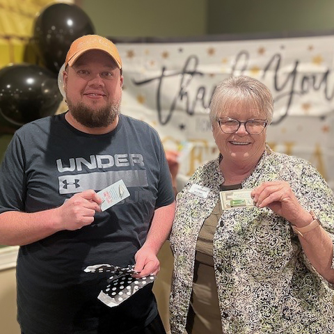 A man and woman on the Wildwood Senior Living team smile while displaying enamel pins gifted in gratitude.