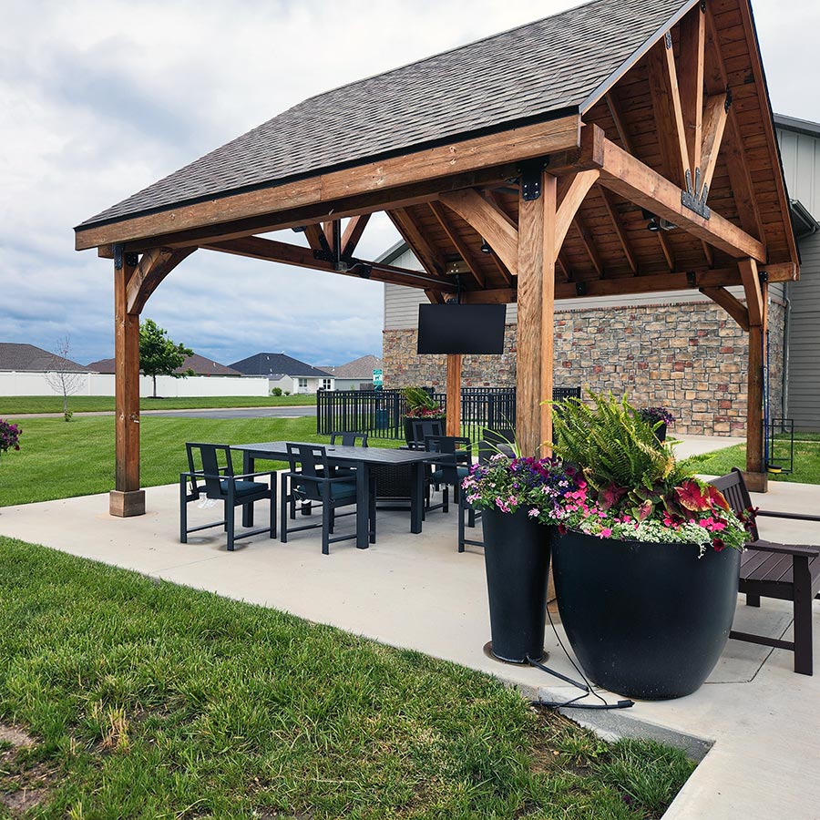 A large wooden gazebo covers a sitting area, decorated with large planters filled with flowers.