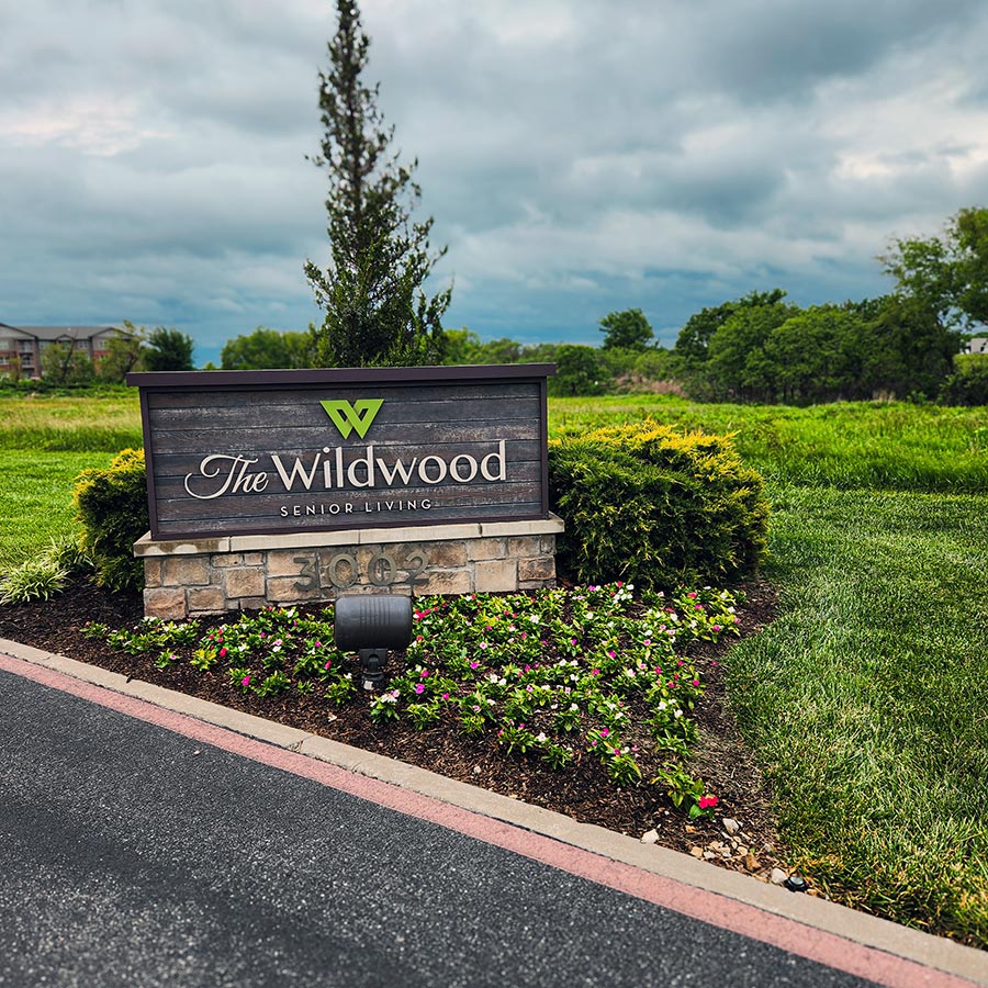 The exterior sign for The Wildwood Senior Living, surrounded by beautifully maintained plants and flowers.